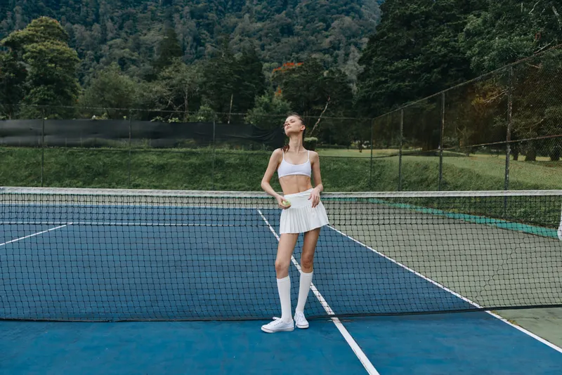 Young athletic woman in sporty tennis outfit posing confidently on a tennis court, showcasing summer vibes and a healthy lifestyle with vibrant green background