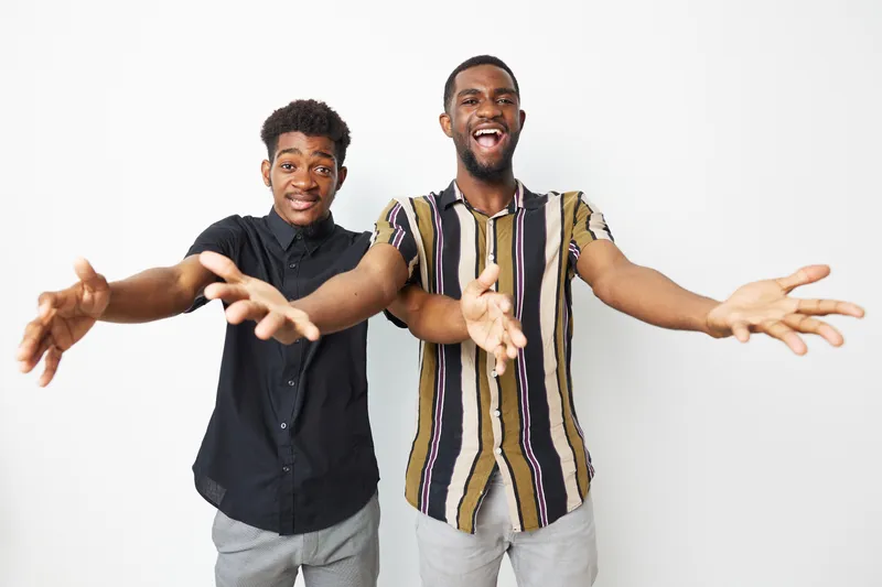 Two smiling African American men joyfully reaching out, showcasing camaraderie and friendship in a bright and cheerful atmosphere.