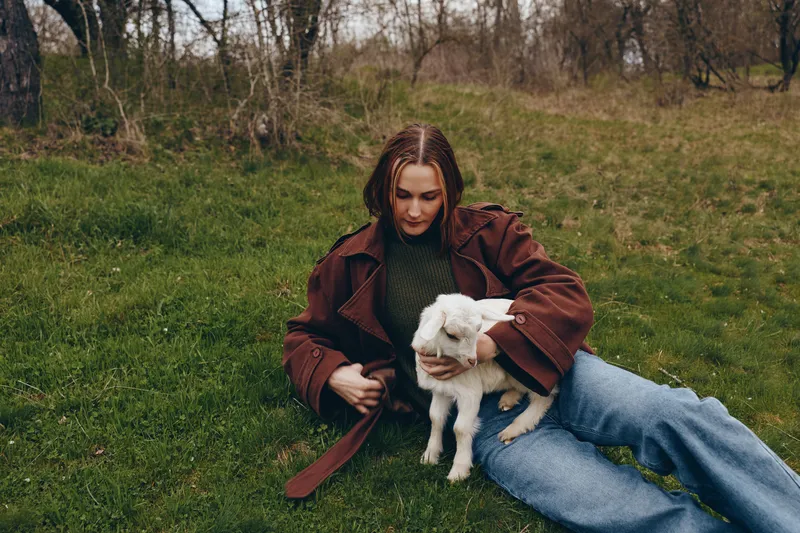 Relaxed woman sitting on grass with a goat kid in a rural park, capturing a wholesome countryside lifestyle, gentle companionship, and a heartwarming bond with nature.