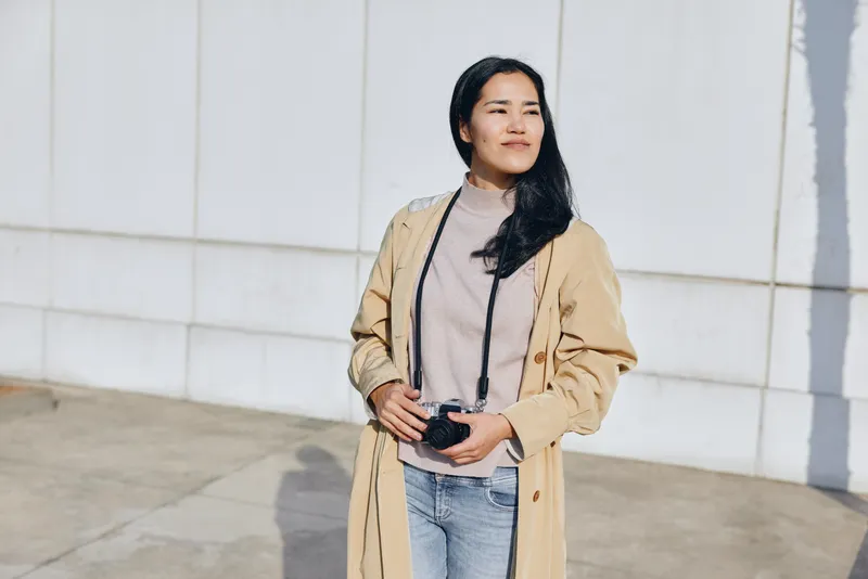 Woman with camera outdoors in a casual fashion look wearing a coat on the street, capturing lifestyle moments with confident pose and natural light