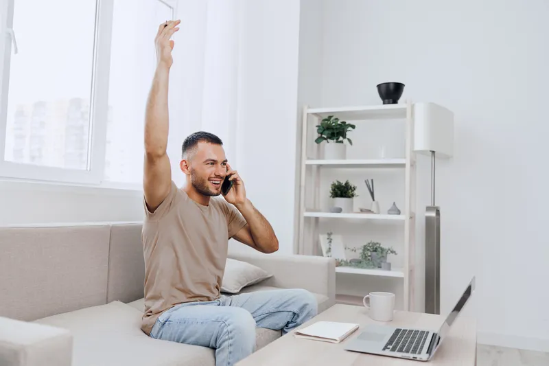 Happy man on a phone call, celebrating a conversation. Showcasing the blend of personal and work life in a cozy home setting, balancing emotions and technology.