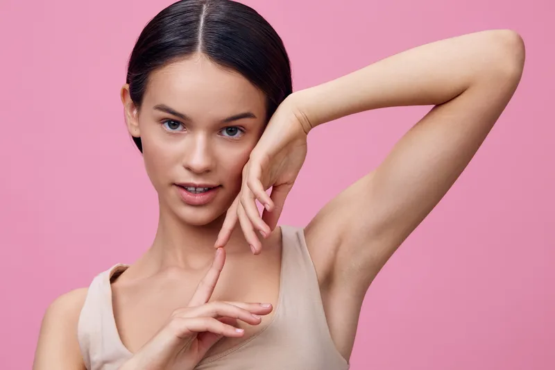 Portrait of a confident young woman with fair skin and long dark hair against a pink background, showcasing beauty and self expression through fashion