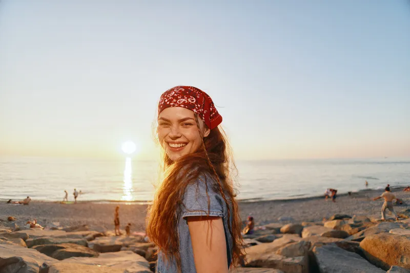 smiling woman in modern boho-western denim street style at the beach during golden hour with film color warmth and natural sunlight