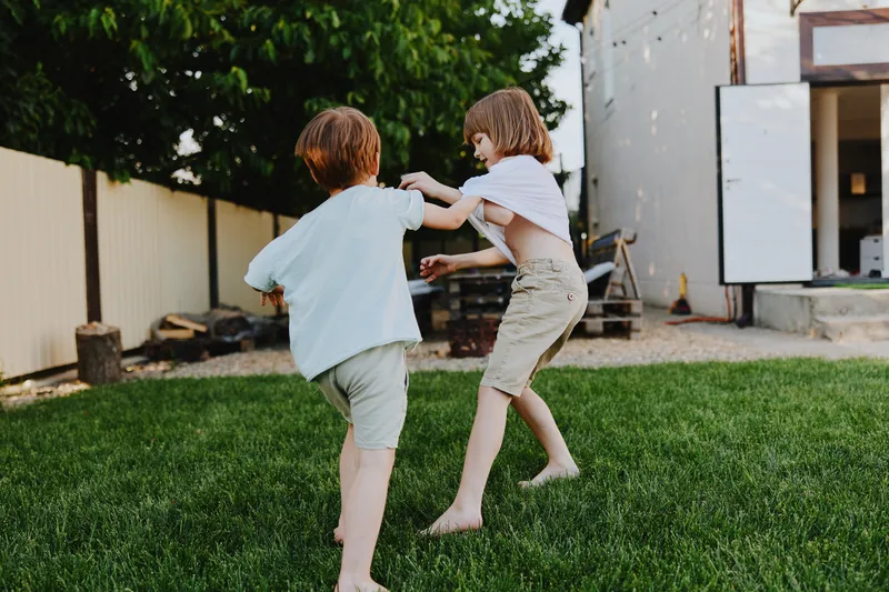 Two playful children running in the garden, enjoying their carefree summer day, engaged in a joyful game of tag with laughter and excitement in the air.