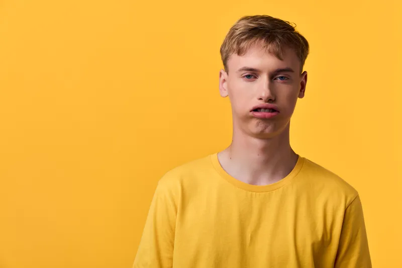 Young man wearing a yellow tshirt stands against a bright yellow background, neutral expression, casual studio style with bold color and clean simple composition