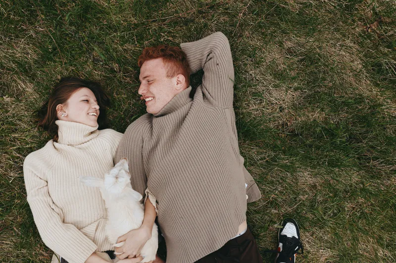 couple outdoors lifestyle cozy grass goat kid laughter affection sunlit breeze natural colors candid composition intimate moment warm