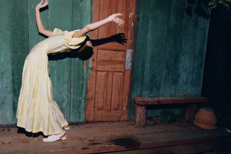 woman in yellow dress bending back in dramatic dance pose by door with shadow authenticity inclusivity