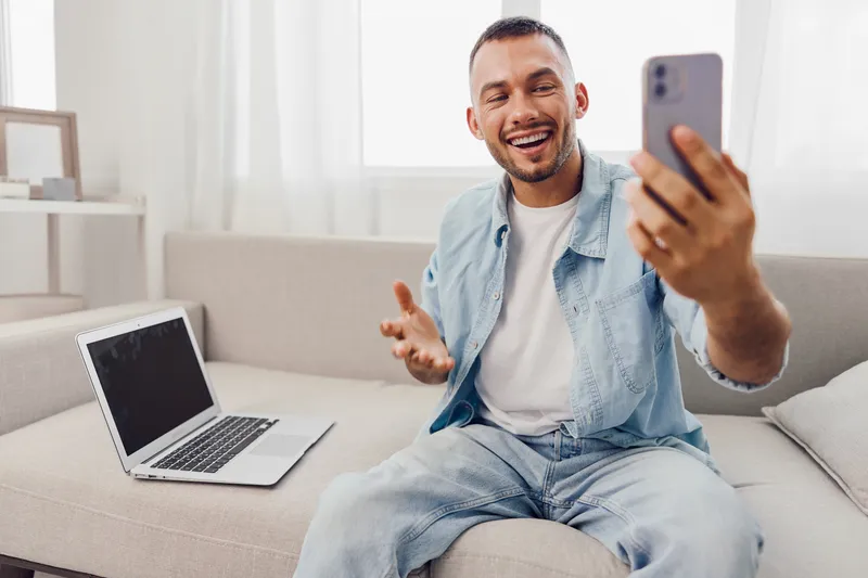 Smiling man engaged in a video call, dressed casually, showcasing modern home office setup. Bright and inviting atmosphere promotes connection and productivity.