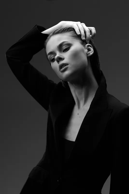 Black and white portrait of a thoughtful woman wearing a blazer with hand on head expressing elegance and introspection.