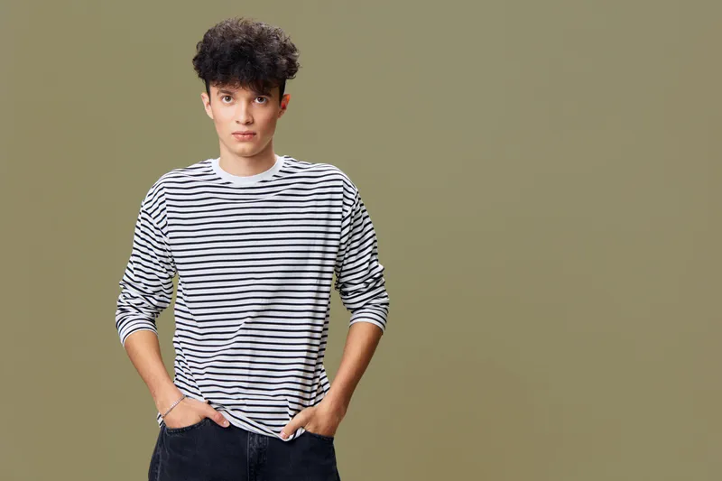 young man in striped shirt standing confidently with hands in pockets against plain beige background in casual style and relaxed pose