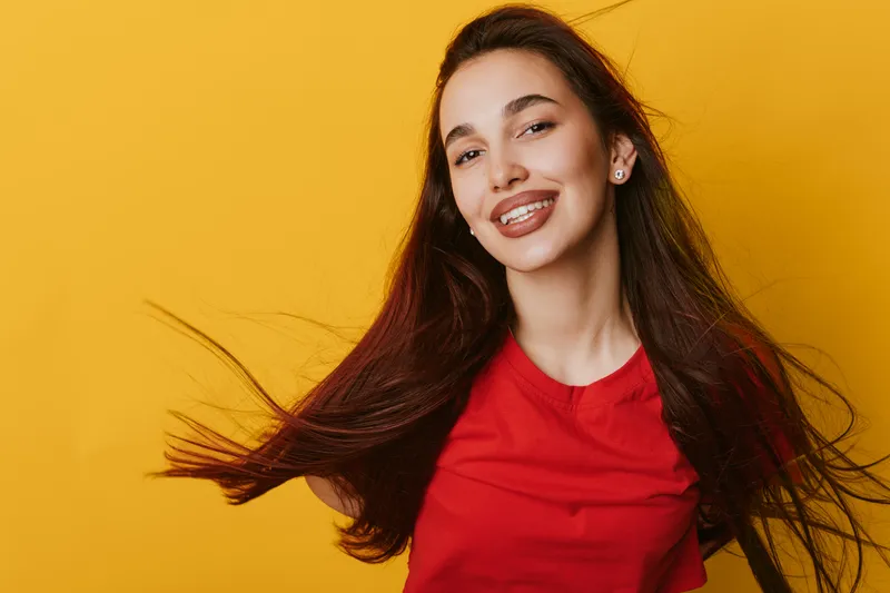 Young woman with long hair smiling and wearing red shirt on yellow background. Portrait of happy female with natural makeup and confident expression in studio lighting.