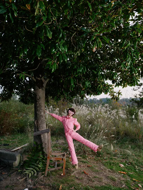 Balance, outdoor, woman, playful, pink jumpsuit, tree, nature, posing in a countryside setting with sunlit meadow, capturing leisure and carefree athletic vibe in a scenic outdoor moment for stock use