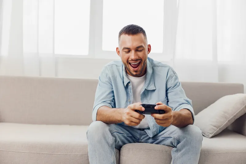 Happy man enjoying a digital detox while playing games on his phone, showcasing a moment of relaxation and engagement with technology at home.