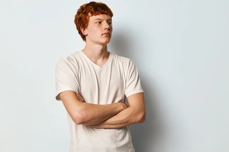 Young man with red hair wearing white t shirt standing with crossed arms looking to side isolated on white background confident casual lifestyle portrait.