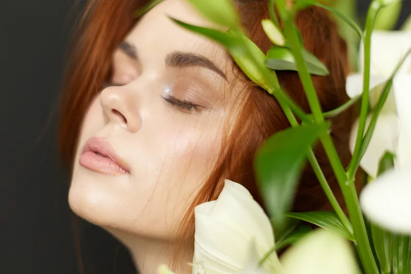 Elegant portrait of a model with red hair surrounded by white flowers, showcasing natural beauty and serenity in a soft color palette