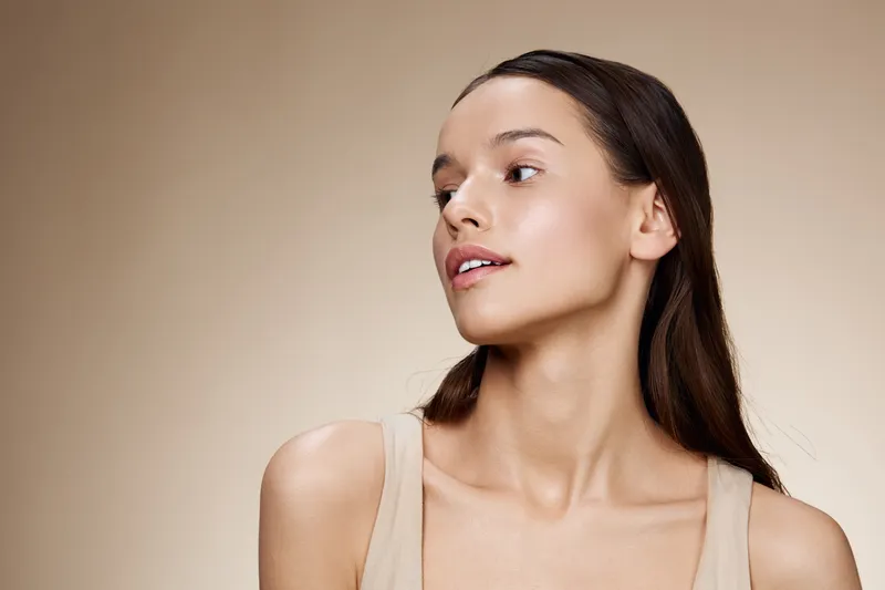 Natural beauty portrait of a young woman with fresh skin, subtle makeup, and a neutral background, conveying confidence and elegance, ideal for wellness and skincare concepts