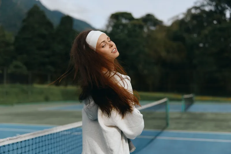 Young woman in sportswear smiling on a tennis court, showcasing healthy lifestyle, athletic spirit, and joyful emotions with vibrant green background