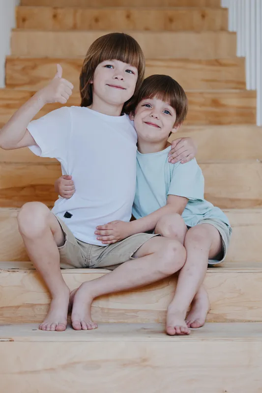 Happy brothers sitting together on wooden stairs, enjoying a playful moment and sharing smiles. This warm family scene captures the essence of childhood joy and connection.