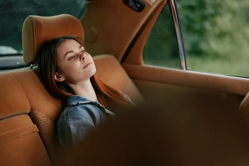 Relaxed young woman with long auburn hair lounging in a car, surrounded by a serene green background, evoking a sense of peace and tranquility.