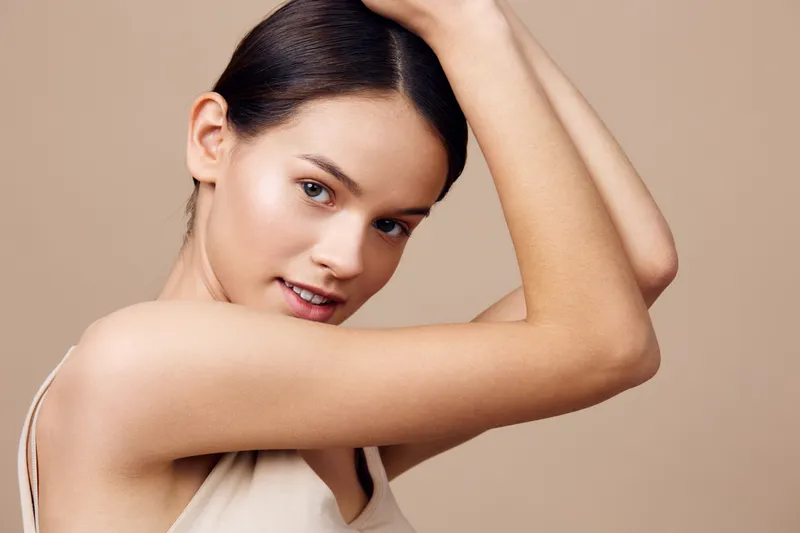 Young woman with smooth skin and natural makeup, posing against a neutral background, conveying confidence and beauty in a minimalist aesthetic