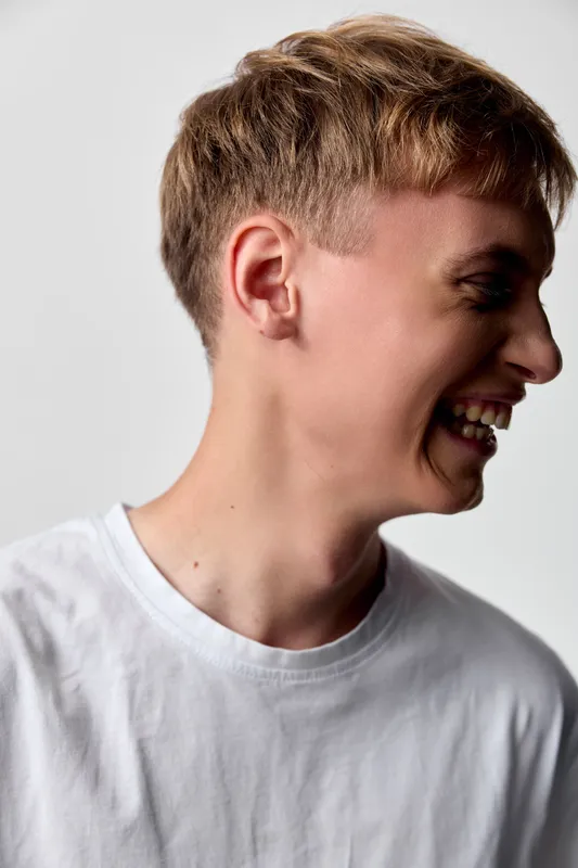 Smiling man in a white t shirt is captured in a studio with a side profile, conveying casual happiness and relaxed mood suitable for lifestyle and fashion stock