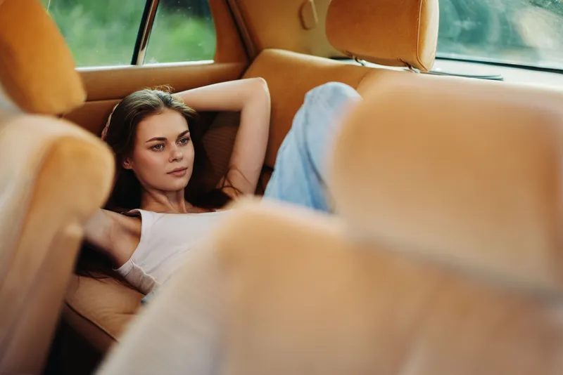Relaxed young woman lounging in a vintage car interior, showcasing comfort and serenity with soft colors and natural light.