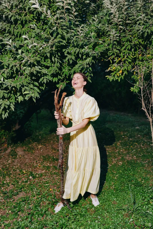 woman dress outdoors nature joyful stick smile garden, woman in yellow dress holding a branch in garden, laughing eyes closed with authenticity inclusivity sunlight
