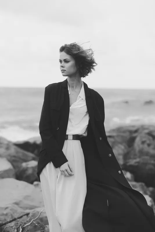 Fashion, style, coastal, wind, sea, monochrome, outfit, coat, dress, elegance convey a windswept look of a chic model along a rocky shore, moody ocean backdrop and timeless wardrobe capturing refined
