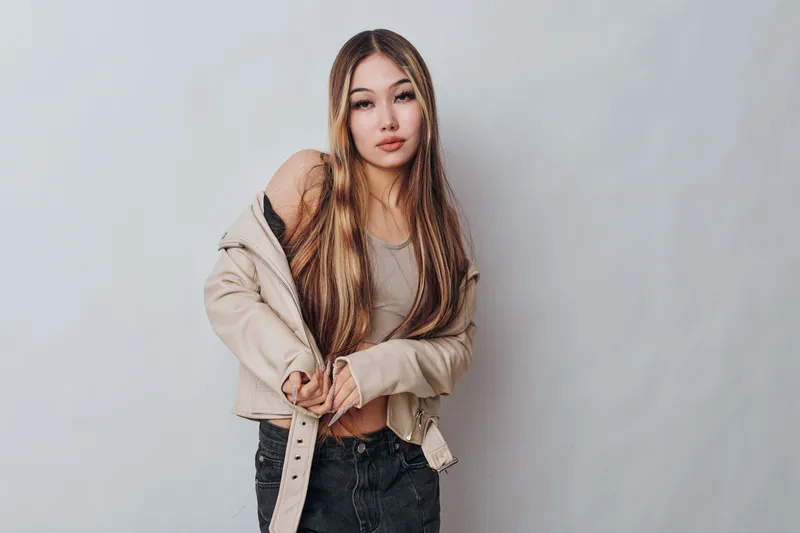 Young woman with long hair wearing casual jacket and tank top standing against grey background for fashion, portrait, beauty and style concept in studio.