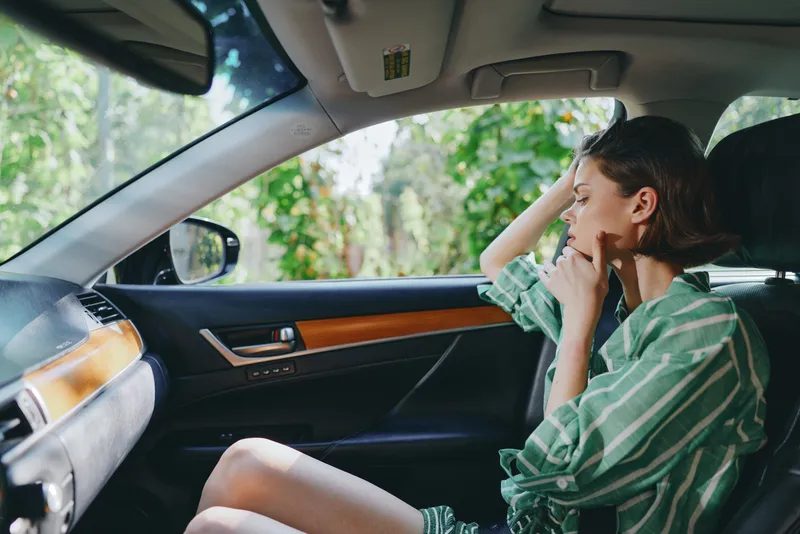 A woman sits in a car interior, gazing out the window with a thoughtful expression.