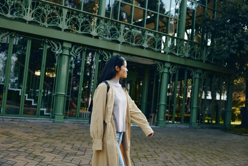 Coat, woman, outdoor, fashion, autumn, urban, casual, elegance, walking beside glass structure in a stylish candid moment showcasing relaxed style and seasonal apparel
