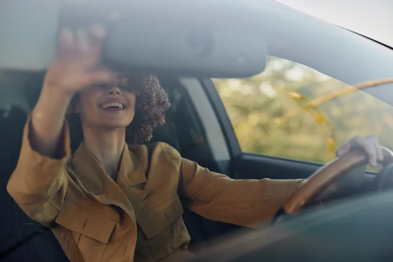 Smiling woman driving a car with retro film color tones, close-up of the interior bathed in warm sunlight, conveying lifestyle, travel, happiness, and personal freedom.