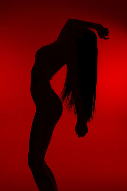 Silhouette of a woman sport fitness posing with arched back against a red background, showcasing body flexibility and strength in a dramatic light.