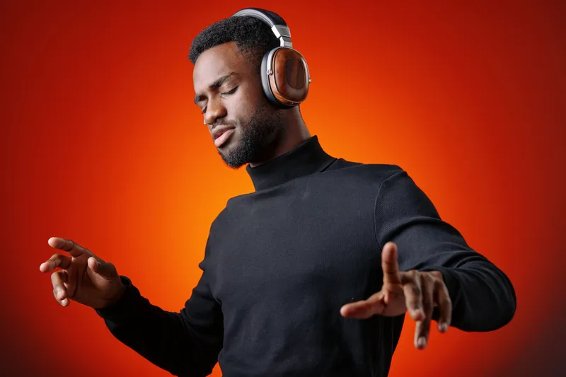 Young Black man enjoying music with headphones, dancing in a stylish black turtleneck against a vibrant orange background Emotions of joy and relaxation