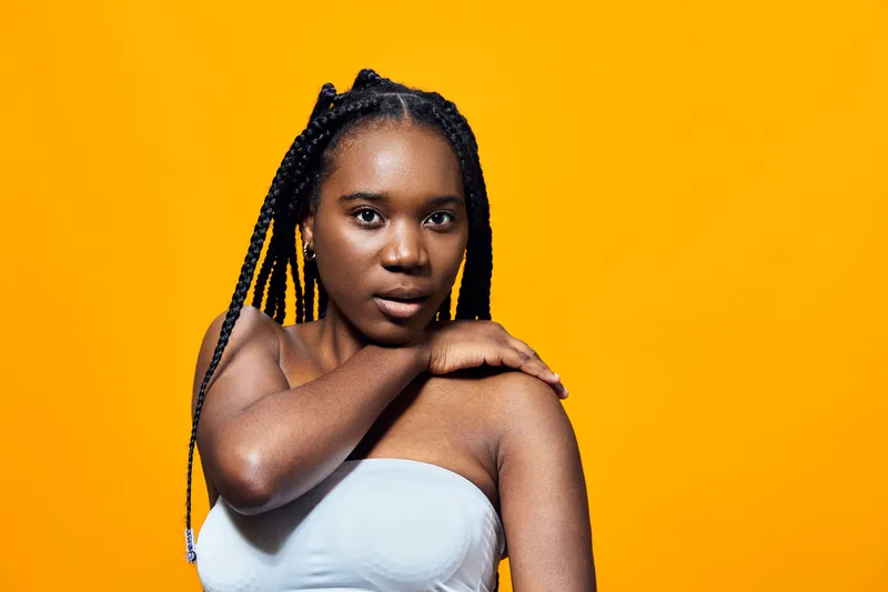 Young woman with braided hair in strapless top, posing confidently against vibrant yellow background, showcasing beauty and self expression, perfect for lifestyle brands