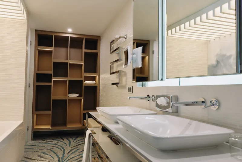 Bathroom vanity with double sinks, modern mirror and organized shelving; neutral tones, spacious layout, soft lighting, and a clean contemporary interior.