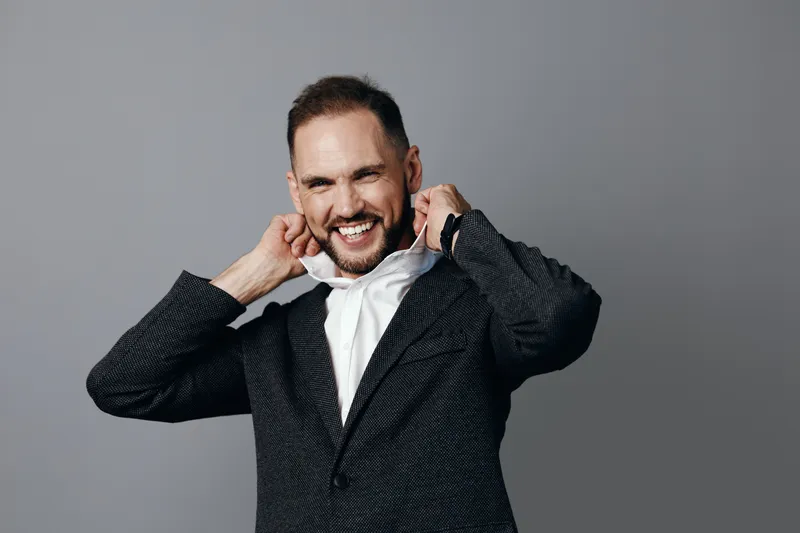 A confident business professional stands on an isolated colored background, adjusting his collar with a friendly smile, conveying approachability, focus, and poised energy for success.