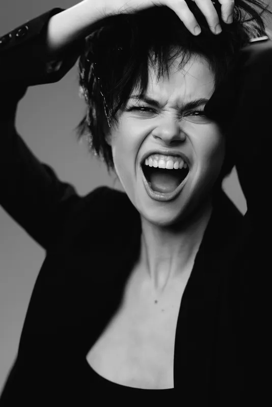 Black and white portrait of a screaming woman with short hair expressing strong emotion and passion in a dramatic close-up.