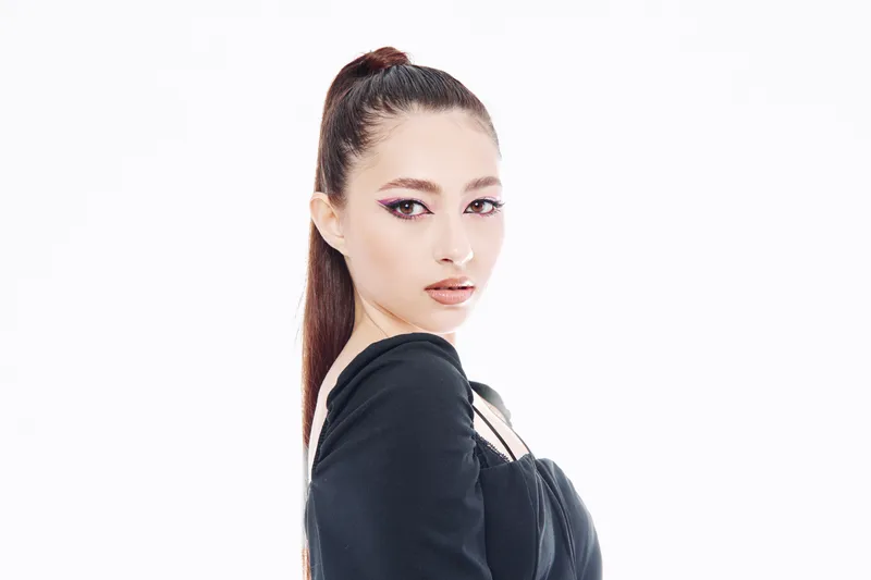 Young female model with sleek hair and bold makeup poses in a stylish black outfit on a white background. Creative fashion beauty concept with dramatic eyeliner.