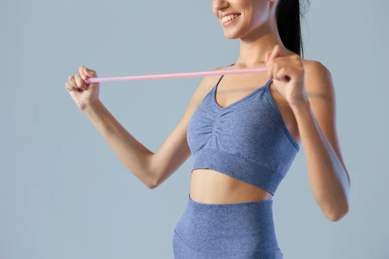 Young woman sport fitness stretching with resistance band wearing blue activewear, healthy lifestyle concept, focus on upper body and exercise equipment.