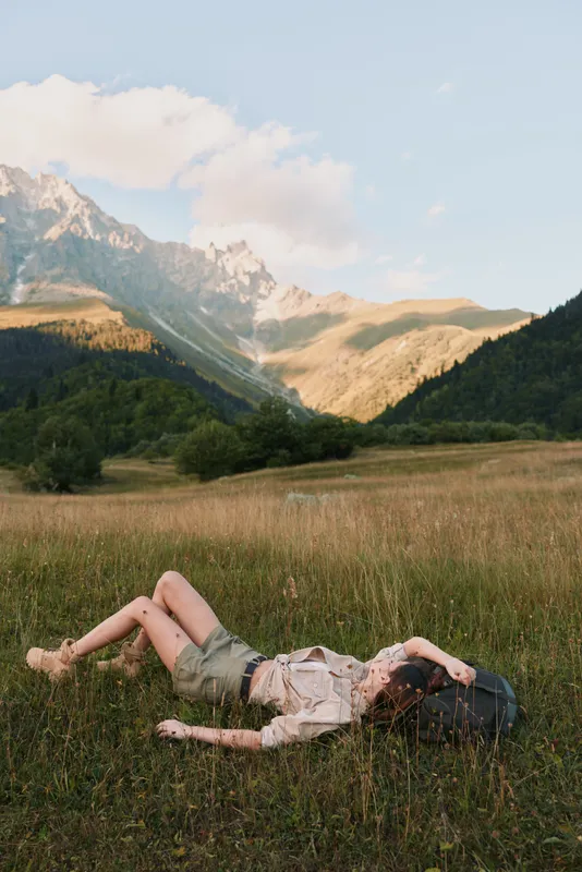 Young woman lying on grass in a mountain valley during daytime, enjoying nature and relaxation. Concept of lifestyle, outdoor leisure, and peaceful moment.
