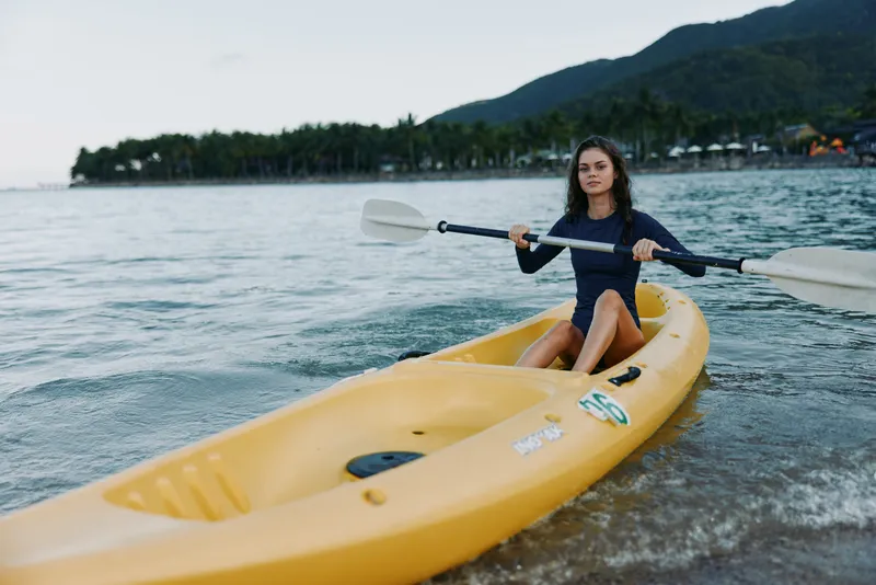 A lone kayaker paddles a bright yellow kayak along a calm shoreline, capturing a moment of adventure, focus, and connection with water and sky.
