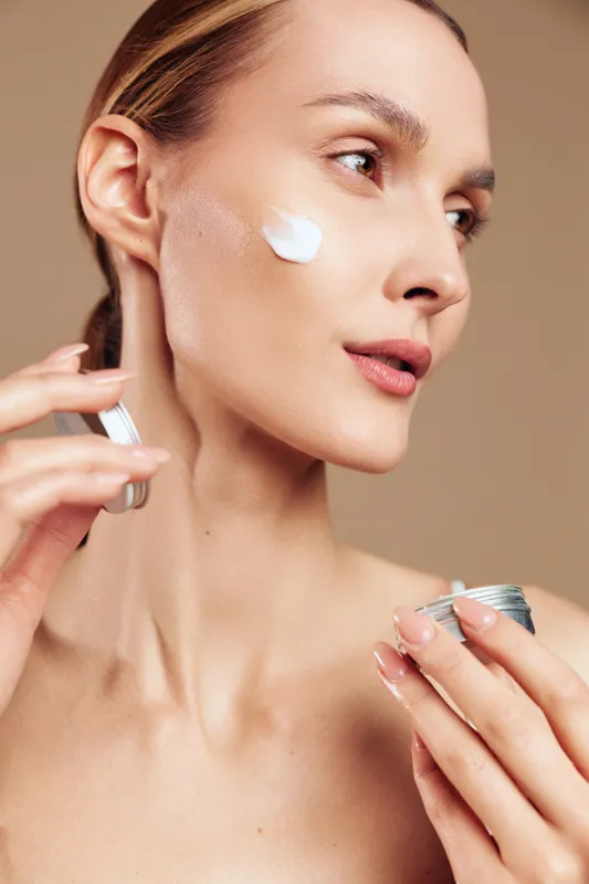Woman applying white face cream with fingertips, closeup portrait, smooth skin and makeup, soft studio lighting on brown background, skincare and self care concept wellness routine