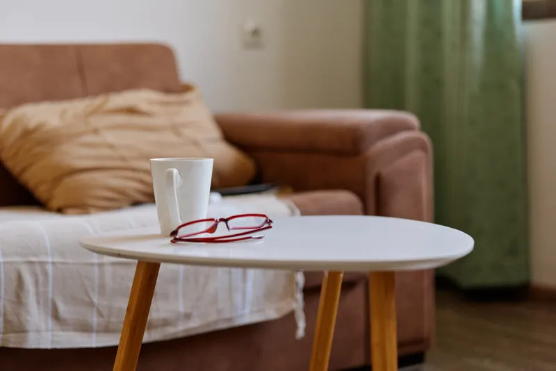 Cozy living room scene with a white mug on a round table, red glasses nearby, soft sofa and calm home ambience with simple modern decor.