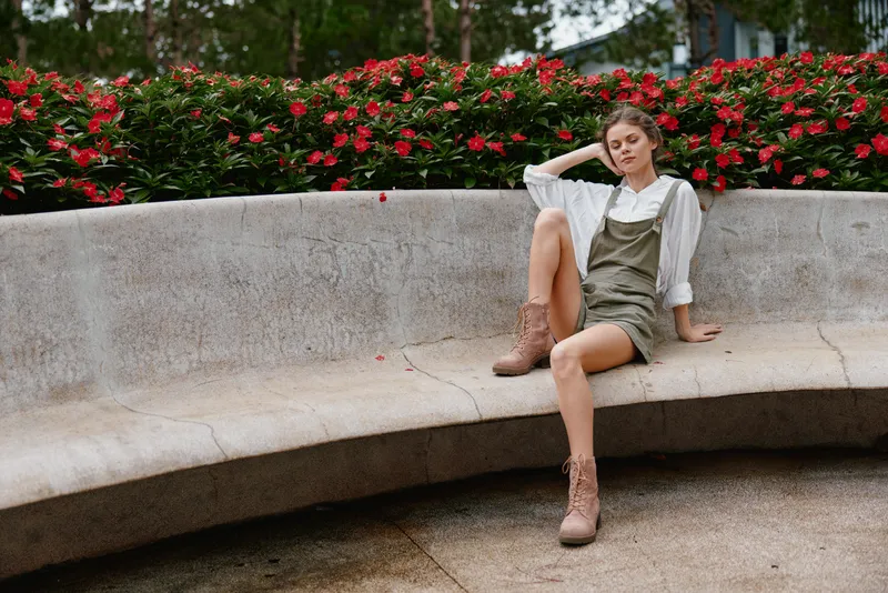 Young woman in casual attire sitting on a curved bench surrounded by colorful flowers, expressing relaxation and confidence in a vibrant outdoor setting