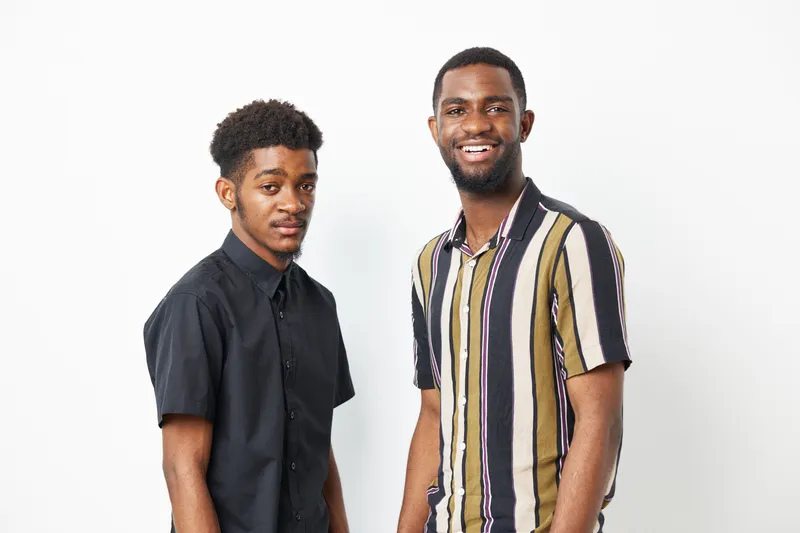 Two black men smiling confidently, dressed in stylish shirts, representing friendship and diversity. Their positive energy reflects joyful moments together.