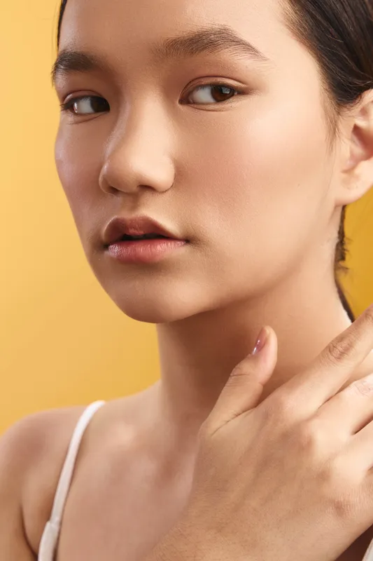 asian woman is featured in a warm studio setting, showcasing clear skin and subtle makeup, exuding calm confidence and modern beauty that feels approachable and fresh.
