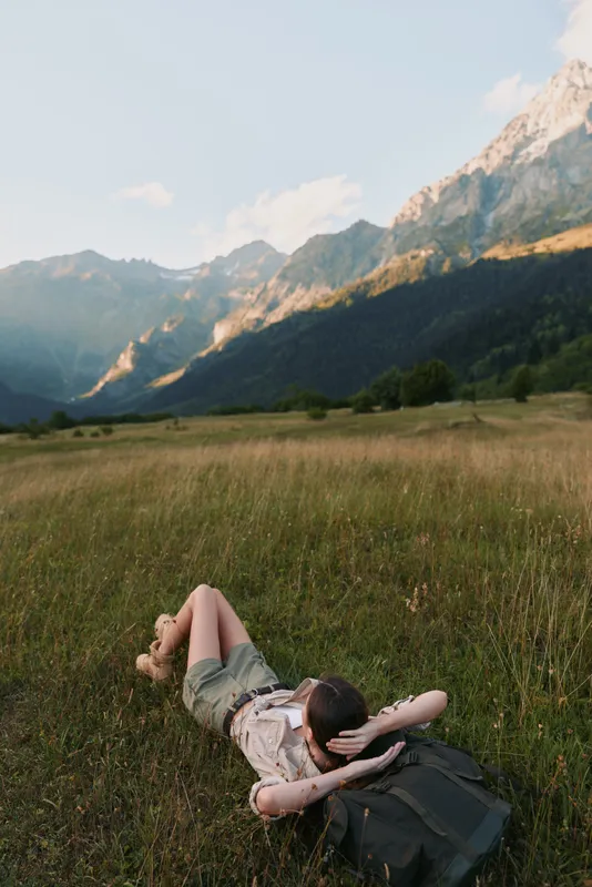 Young woman with long hair lies on grass in a mountain meadow enjoying a peaceful moment during a sunny day.