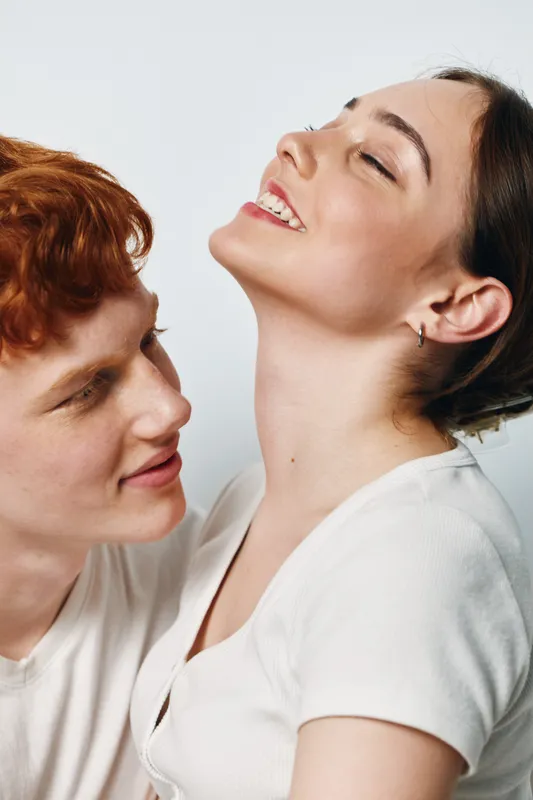 Couple, young, smiling and happy with tenderness for relationship and love. Man with red hair looks at woman who is closing eyes and enjoying moment together in white shirts.