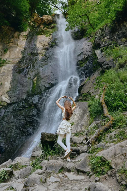 woman near waterfall in forest nature scene, standing on rocks surrounded by lush greenery and flowing water, peaceful and adventurous atmosphere